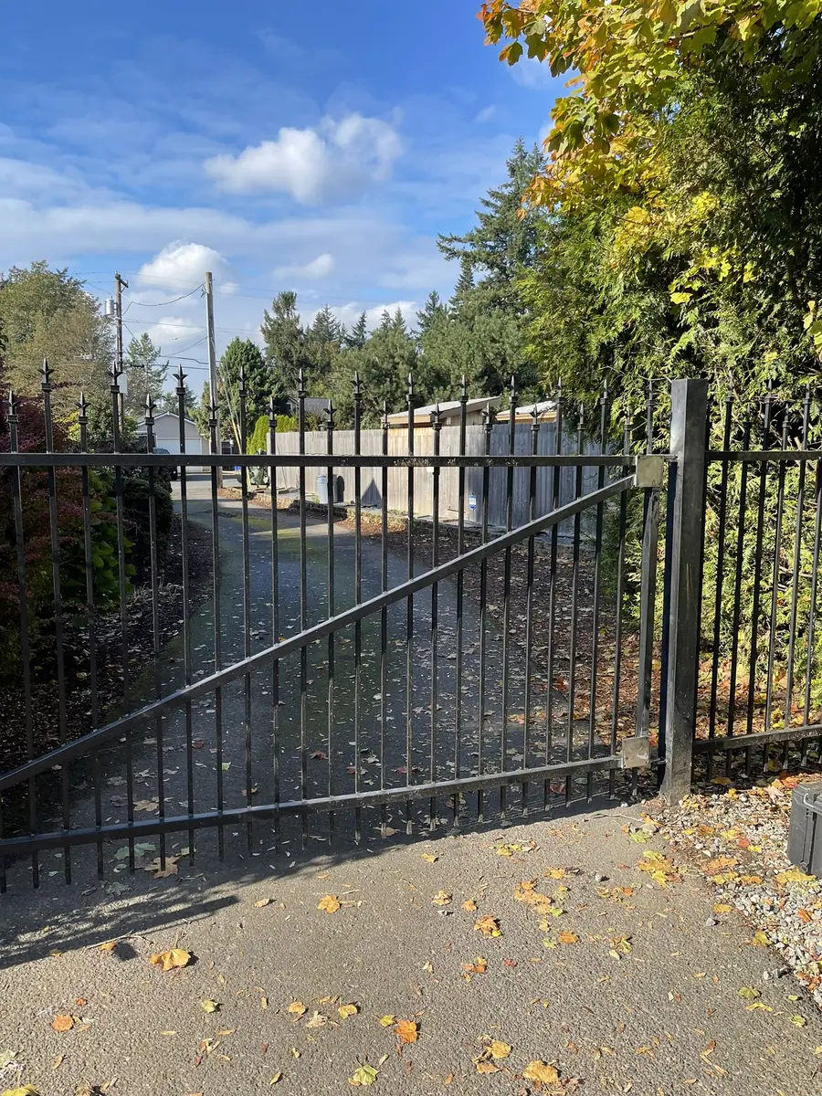 Black steel driveway gate on steel posts, closed across a paved driveway