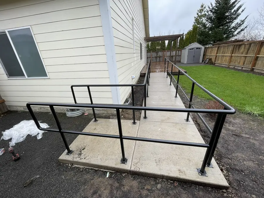 Black steel handrails on both sides of a concrete ramp beside a house