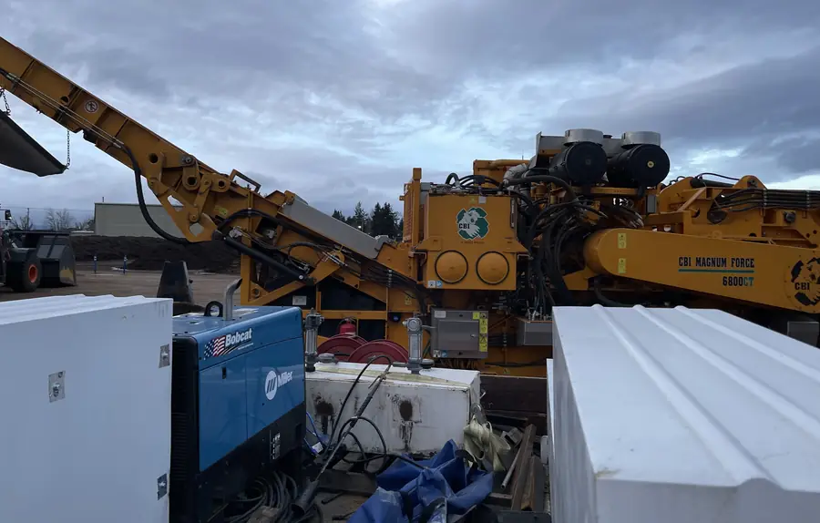 Neal's welder set up in front of a big wood grinder at a recycling yard